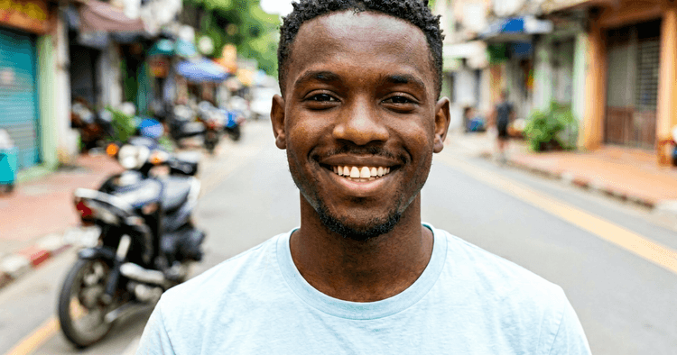 young black African man in a shirt on a street in Mozambique, with a delivery motorcycle blurred in the background, bust portrait, no legible text