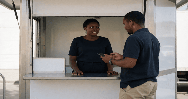 Agente de mobile money num quiosque ao ar livre a ajudar um cliente com o telemóvel