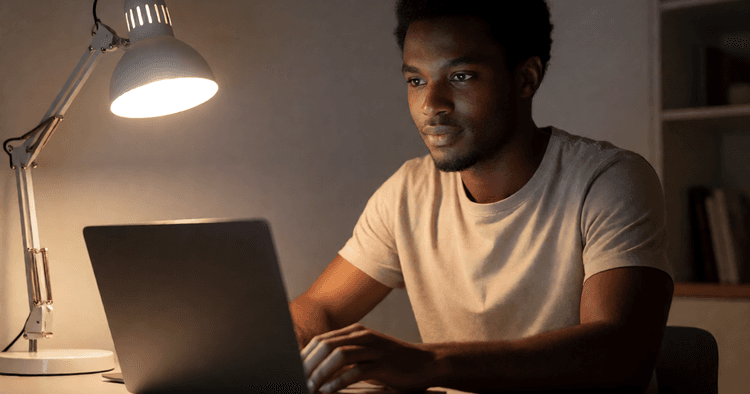 Mozambican worker in night home office with desk, lamp, and laptop with screen off