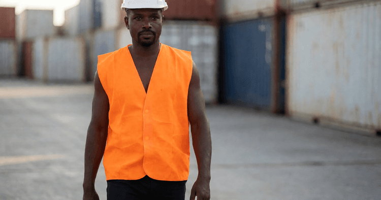 Trabalhador moçambicano a caminhar num pátio industrial com contentores ao fundo