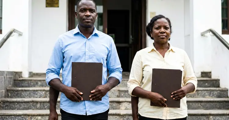 two people entering official building carrying folders, exterior