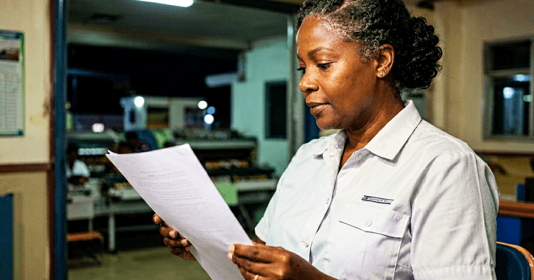 Mozambican female worker on factory night shift, checking the shift schedule on the gantry, no readable text