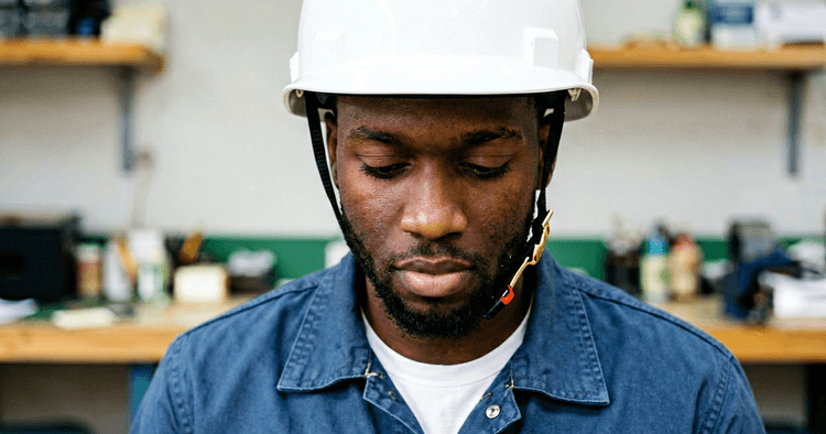 young Mozambican intern focused in an industrial workshop, plain white hard hat and work uniform, chest-up portrait, no legible text