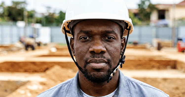 Mozambican man in white helmet at a construction site, chest-up portrait, no legible text