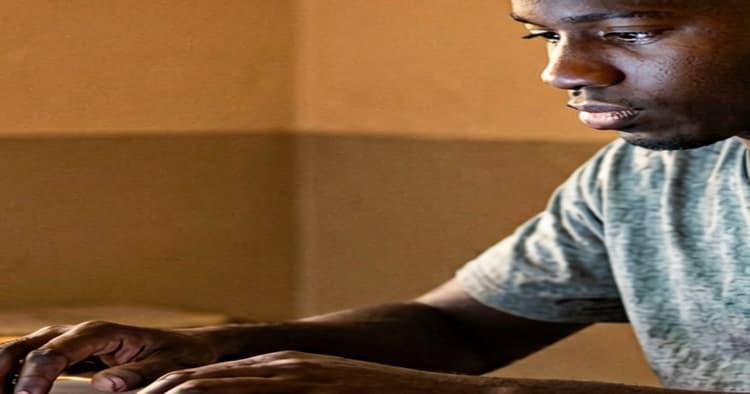 Young Mozambican woman working on a laptop in a simple room, remote work session